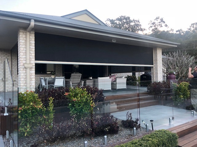 Motorised patio screen being lowered over an outdoor entertaining area at dusk